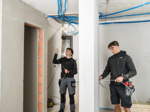 Zwei Elektroinstallateure beim Kabeleinzug auf einer Baustelle für die Stromversorgung.