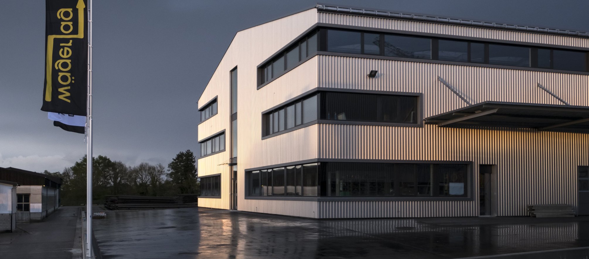 Aussenansicht des Firmengeb&auml;udes der Elektro W&auml;ger AG mit Fahnen bei Abendd&auml;mmerung