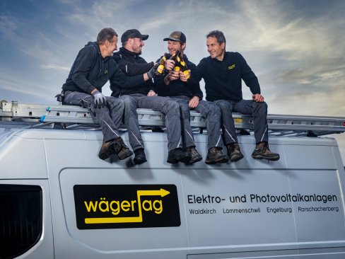 Vier Mitarbeitende der Elektro Wäger AG stossen auf dem Firmenfahrzeug gemeinsam an