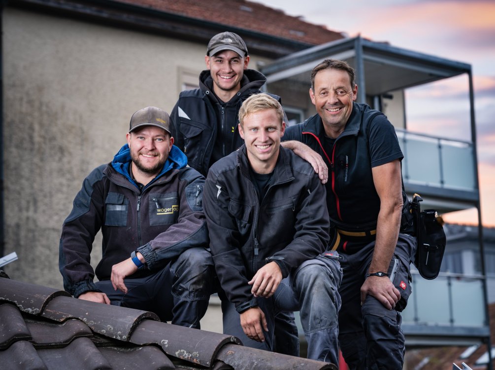 Vier Mitarbeitende der Elektro Wäger AG posieren für ein Teamfoto auf einem Dach