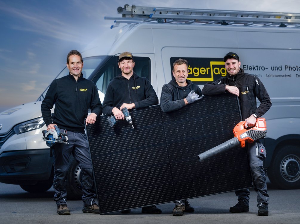 Vier Mitarbeitende der Elektro Wäger AG mit Photovoltaikmodul vor Firmenfahrzeug